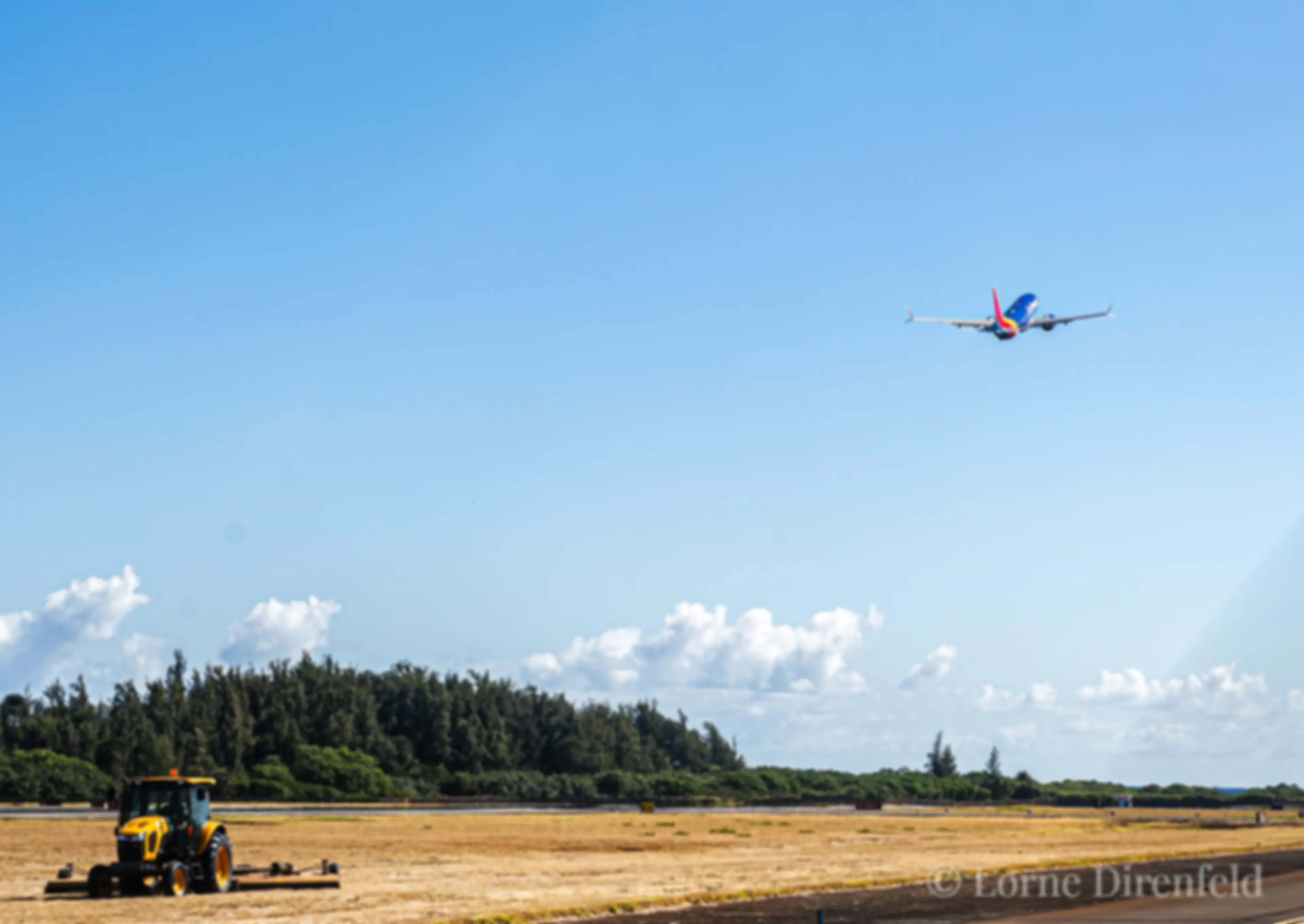 A beautiful morning at the Kahului airport, as a Southwest B737 is taking off into a beautiful blue sky, while the grass cutter tends the areas between the runway and taxiway . . .